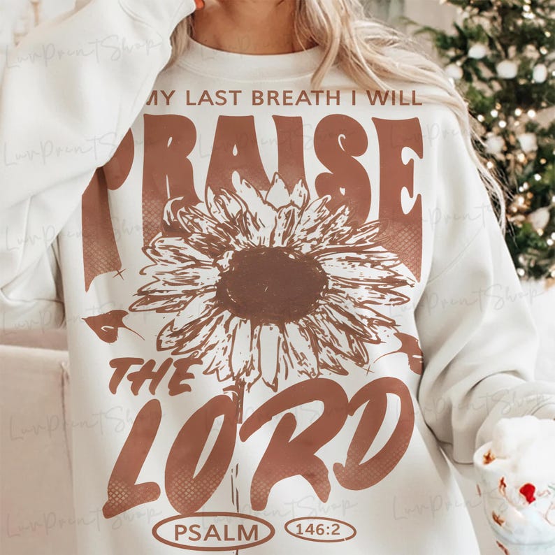 May include: Cream-colored sweatshirt with a large brown sunflower graphic and the words "MY LAST BREATH I WILL RAISE THE LORD" in brown. The text "PSALM 146:2" is printed at the bottom. A cozy and inspirational design.