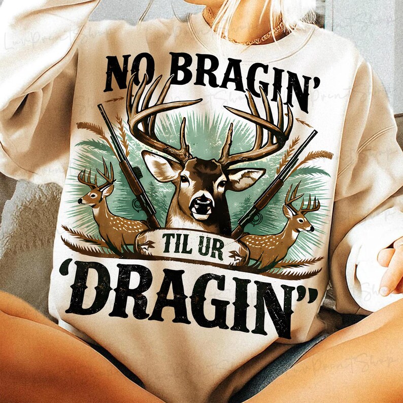 May include: Cream-coloured sweatshirt featuring a deer graphic and the text "NO BRAGIN' TIL UR DRAGIN'". The design includes deer, rifles, and a banner. The sweatshirt is a casual style.