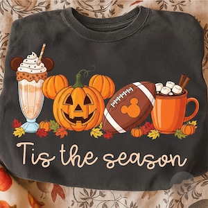 May include: Dark grey sweatshirt featuring a seasonal graphic. The design includes a milkshake, a carved pumpkin, a football, and a mug of hot chocolate. The text "Tis the season" is written in a cursive font.