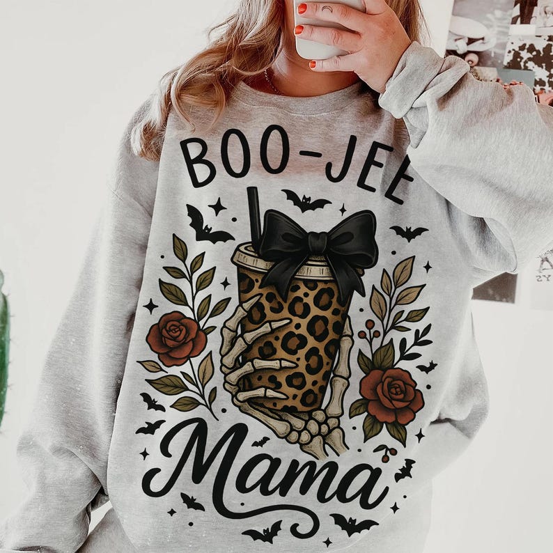 Op de afbeelding: Een lichtgrijze sweatshirt met een Halloween-thema. Het ontwerp toont de woorden "BOO-JEE Mama" met een beker met luipaardprint die wordt vastgehouden door een skelet hand, een zwarte strik, vleermuizen en rozen.