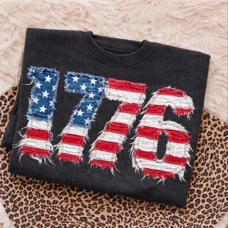 May include: Dark gray sweatshirt with the number "1776" appliqued on the front. The numbers are designed to resemble the American flag, with blue star fields and red and white stripes.