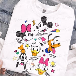 Puede incluir: Sudadera blanca con ilustraciones de dibujos animados de Mickey Mouse, Minnie Mouse, Donald Duck, Daisy Duck, Goofy y Pluto. El dise&ntilde;o incluye estrellas, corazones y los nombres de los personajes.