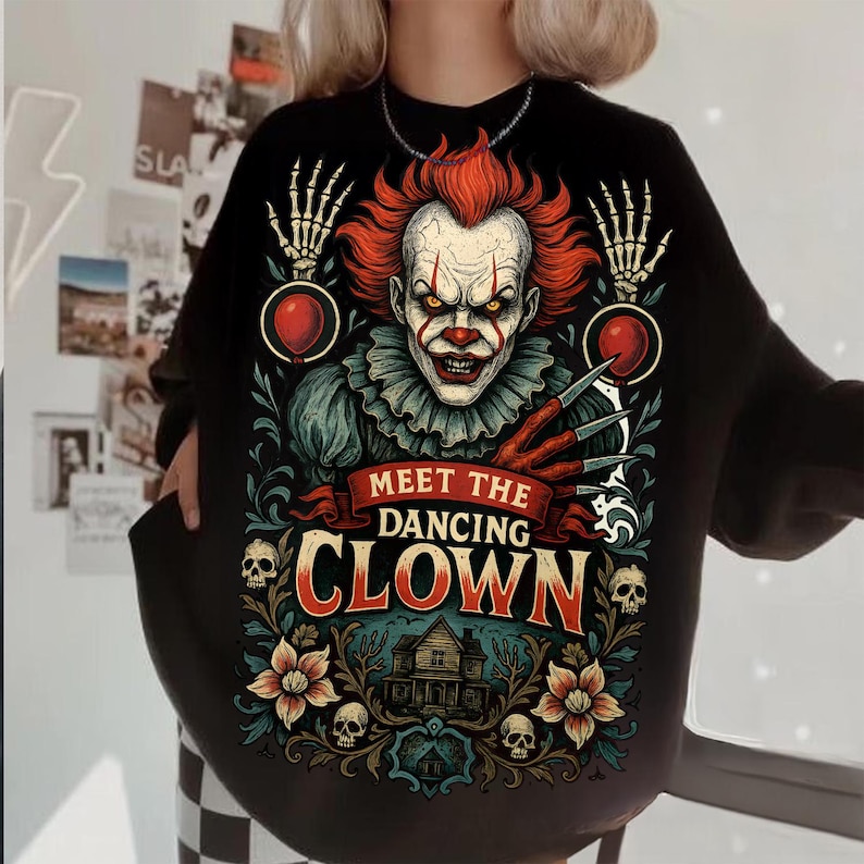 May include: A black long-sleeve sweatshirt featuring a graphic print of a clown with red hair, sharp claws, and skeleton hands holding red balloons. The text reads MEET THE DANCING CLOWN above a house illustration, skulls, and floral motifs.