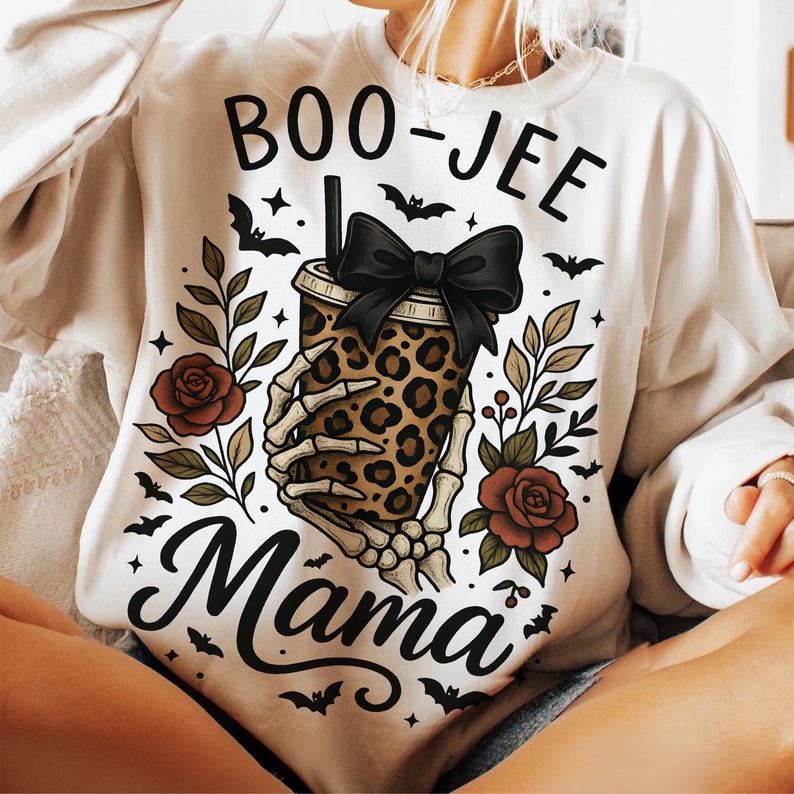 Op de afbeelding: Cr&egrave;mekleurige sweatshirt met een Halloween-thema. Het ontwerp toont een beker met luipaardprint die wordt vastgehouden door een skelet, een zwarte strik, rozen, vleermuizen en de woorden "BOO-JEE Mama".
