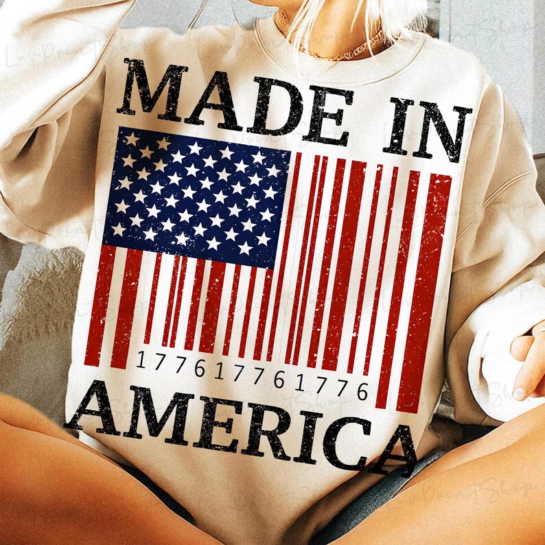 Peut inclure: Sweat-shirt cr&egrave;me avec l'inscription "MADE IN AMERICA" en noir. Le motif repr&eacute;sente un drapeau am&eacute;ricain stylis&eacute; avec un motif de code-barres &agrave; rayures rouges et blanches, et un champ d'&eacute;toiles bleu.