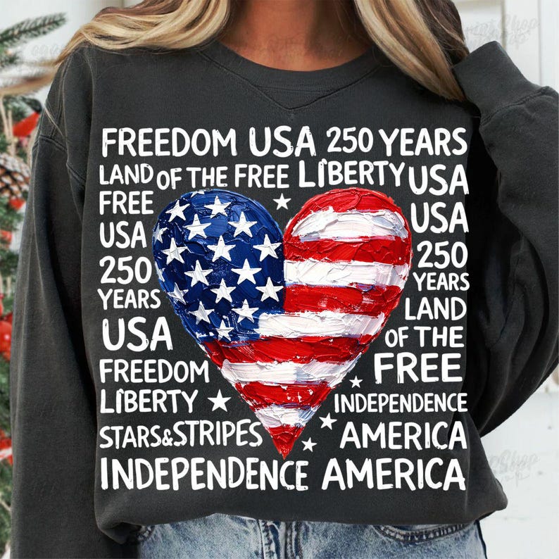 Puede incluir: Sudadera gris oscuro con un dise&ntilde;o de bandera estadounidense en forma de coraz&oacute;n. El coraz&oacute;n est&aacute; dividido, con estrellas azules a la izquierda y rayas rojas y blancas a la derecha. El texto incluye "Freedom USA 250 Years".