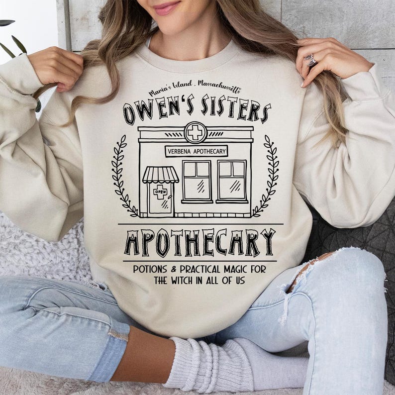 以下が含まれることがあります： 「Owen's Sisters Apothecary」の文字と「Potions & Practical Magic for the Witch in All of Us」のテキストが入った、黒いグラフィックの店舗が描かれたクリーム色のスウェットシャツ。スウェットシャツは長袖で、クルーネックです。