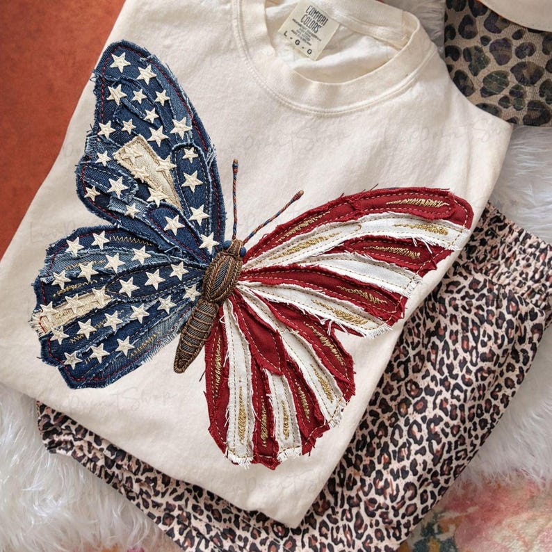 Puede incluir: Camiseta de manga larga color crema con un gran dise&ntilde;o de mariposa. Las alas de la mariposa est&aacute;n hechas de tela vaquera y tela roja y blanca, que se asemejan a la bandera estadounidense. Debajo hay un pantal&oacute;n con estampado de leopardo doblado.