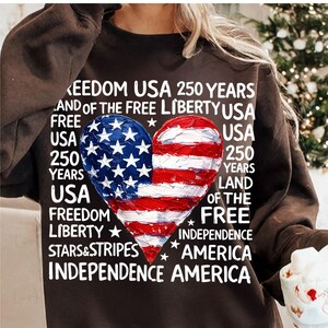 Puede incluir: Una sudadera marr&oacute;n con un dise&ntilde;o en forma de coraz&oacute;n con los colores de la bandera estadounidense. El dise&ntilde;o est&aacute; dividido, con estrellas azules en un lado y rayas rojas y blancas en el otro. El texto incluye "Freedom USA 250 Years".