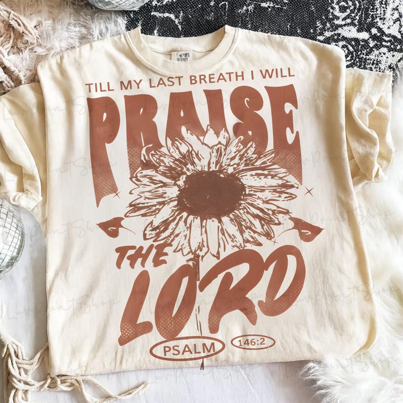 May include: Cream-colored t-shirt with a brown sunflower graphic and text that reads "TILL MY LAST BREATH I WILL PRAISE THE LORD PSALM 146:2". The design is centered on the front of the shirt.