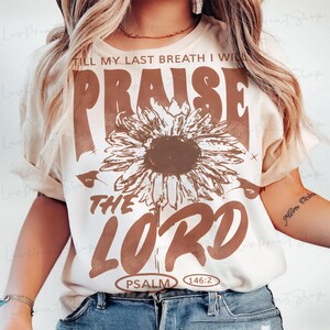 May include: Cream-colored t-shirt with a brown sunflower graphic and the words "PRAISE THE LORD" in a bold, vintage font. The text "TILL MY LAST BREATH I WILL" is above the sunflower, and "PSALM 146:2" is below.