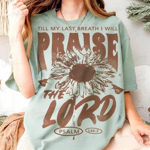 May include: A light green t-shirt with the text "TILL MY LAST BREATH I WILL PRAISE THE LORD" in brown. A large brown sunflower is centered below the word "PRAISE". The text "PSALM 146:2" is at the bottom.