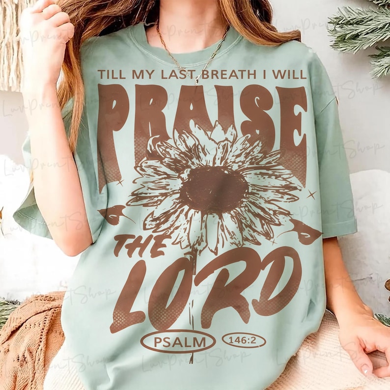 May include: A light green t-shirt with the text "TILL MY LAST BREATH I WILL PRAISE THE LORD" in brown. A large brown sunflower is centered below the word "PRAISE". The text "PSALM 146:2" is at the bottom.