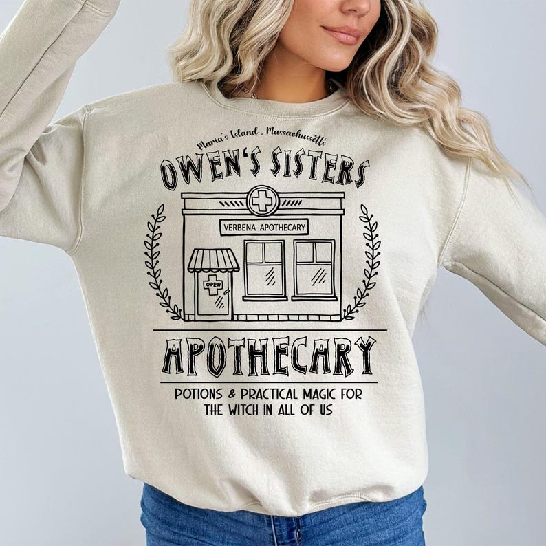 以下が含まれることがあります： クリーム色のスウェットシャツ。黒いグラフィックには「Owen's Sisters Apothecary」と「Maria's Island, Massachusetts」の文字。デザインには店のイラスト、十字のシンボル、そして「Potions & Practical Magic for the Witch in All of Us」というフレーズが含まれています。