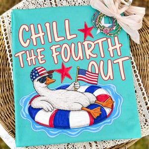 May include: A turquoise t-shirt with the phrase "CHILL THE FOURTH OUT" in red and white lettering. The shirt features a cartoon duck wearing sunglasses and a patriotic hat, floating on a red, white, and blue inner tube, holding an American flag.