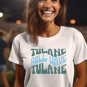 May include: A white t-shirt with a green and blue graphic design that says "Tulane Roll Wave Tulane" in a retro font.