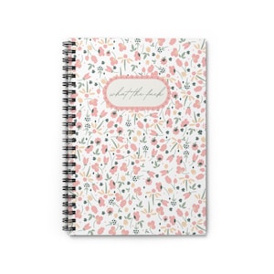 May include: A white spiral notebook with a pink and yellow floral pattern. The text "what the fuck" is written in a black oval on the front cover.