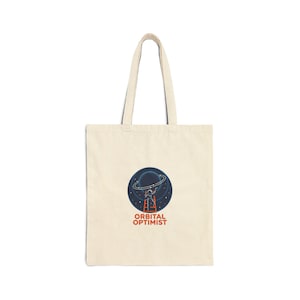 May include: Cream-colored tote bag featuring a circular graphic of a planet with a ring and an astronaut on a ladder. The text "ORBITAL OPTIMIST" is below the graphic. The bag has a simple design with long handles.