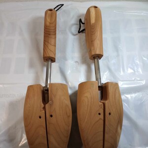 May include: Two wooden shoe trees with metal adjusters. The shoe trees are brown and have a natural wood finish. The shoe trees are designed to help maintain the shape of shoes.