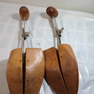 May include: A pair of wooden shoe stretchers with adjustable metal arms. The stretchers are made of light brown wood and have a smooth finish.