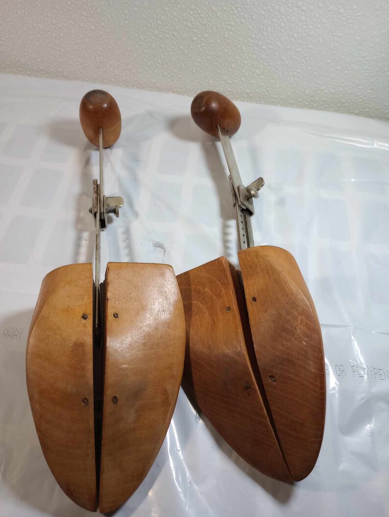 May include: A pair of wooden shoe stretchers with adjustable metal arms. The stretchers are made of light brown wood and have a smooth finish.