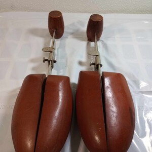 May include: A pair of brown wooden shoe trees with metal adjusters. The shoe trees are designed to help maintain the shape of shoes.