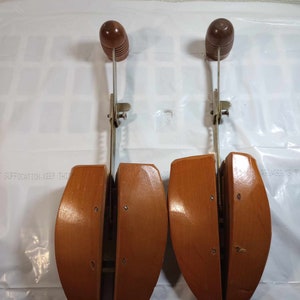 May include: Two wooden shoe trees with metal adjustable arms. The shoe trees are brown and have a rounded shape. The metal arms are silver and have a spring mechanism.