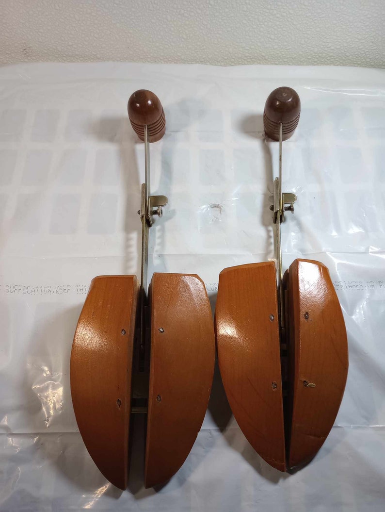 May include: Two wooden shoe trees with metal adjustable arms. The shoe trees are brown and have a rounded shape. The metal arms are silver and have a spring mechanism.
