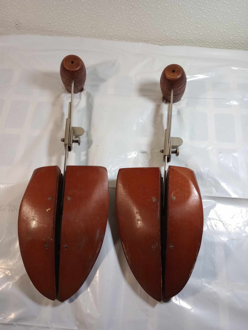 May include: Two wooden shoe trees with metal adjustable arms. The shoe trees are brown and have a rounded shape. The metal arms are silver and have a spring-loaded mechanism.