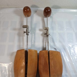 May include: A pair of wooden shoe trees with metal adjustable arms and wooden knobs. The shoe trees are brown and have a split design.