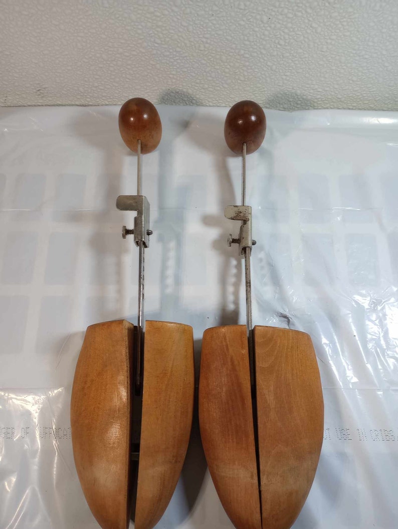 May include: A pair of wooden shoe trees with metal adjustable arms and wooden knobs. The shoe trees are brown and have a split design.