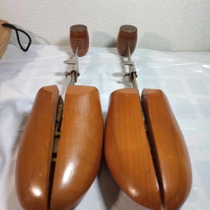 May include: A pair of wooden shoe trees with metal adjusters. The shoe trees are brown and have a smooth finish.
