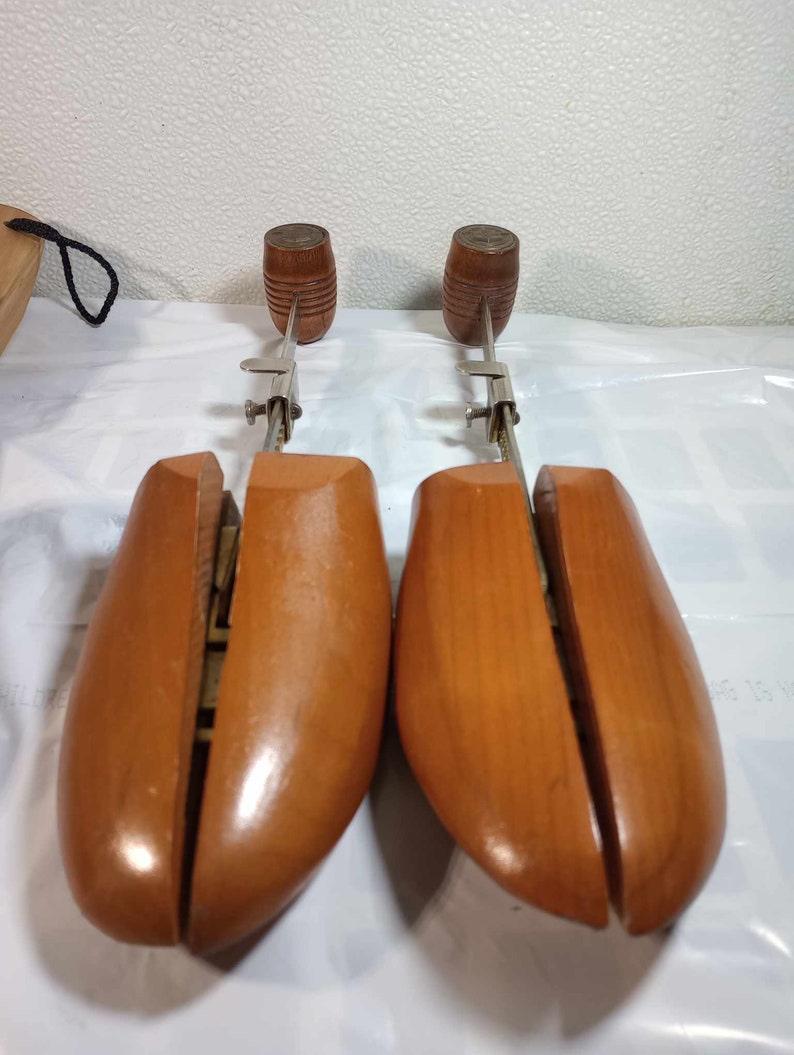 May include: A pair of wooden shoe trees with metal adjusters. The shoe trees are brown and have a smooth finish.