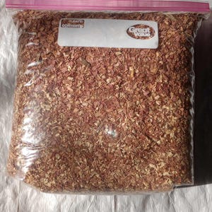 May include: A clear plastic bag filled with reddish-brown wood chips. The bag has a pink zipper closure and a white label with the words "DATE CONTENT" and "Great Value". The bag is sitting on a white, crinkled surface.