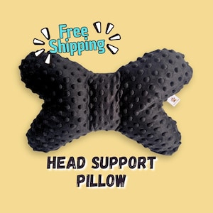 May include: A black, bone-shaped head support pillow with a textured, raised dot pattern across its surface. The pillow features a small white tag on the right side and includes the text Free Shipping and HEAD SUPPORT PILLOW.