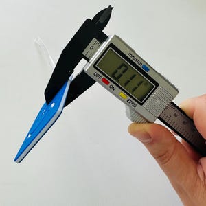 May include: A close-up of a digital caliper measuring a blue and white arrow-shaped object. The caliper reads 0.11 inches.