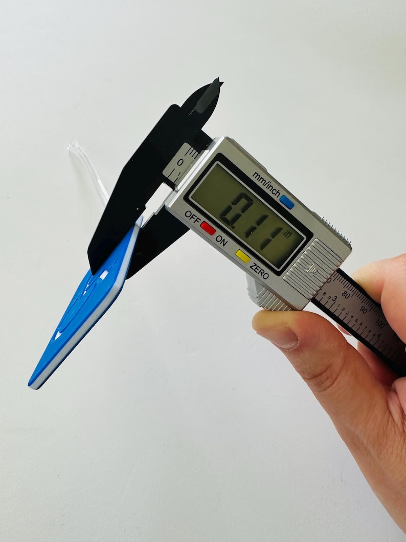 May include: A close-up of a digital caliper measuring a blue and white arrow-shaped object. The caliper reads 0.11 inches.