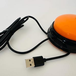 May include: Orange USB foot pedal with a black cord and a USB connector. The pedal is round and has a black rim.