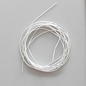 Könnte beinhalten: Nahaufnahme einer Spule aus weißem Faden auf grauem Hintergrund. Der Faden ist dünn und scheint aus synthetischem Material zu bestehen. Die Spule ist ordentlich angeordnet, mit einem einzelnen Strang, der sich nach außen erstreckt.