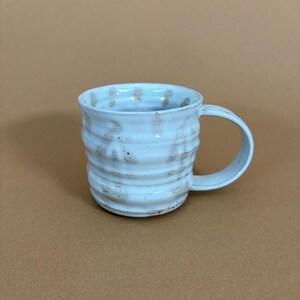 Handgemaakte mok van steengoed, met een wit en beige glazuur met bladmotief.