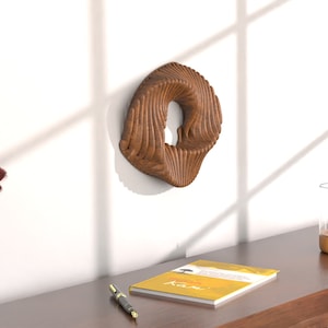 May include: A wooden wall sculpture in the shape of a swirling circle with a hole in the center. The sculpture is mounted on a white wall.