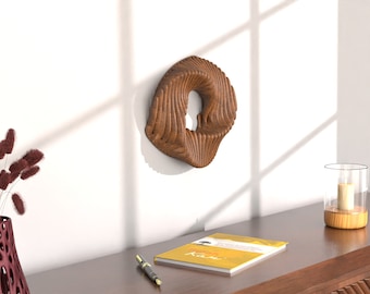 Può includere: Una scultura da parete in legno a forma di cerchio vorticoso con un foro al centro. La scultura è montata su una parete bianca.