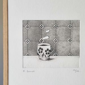 May include: A pencil drawing of a coffee cup with a floral design, with a splash of liquid above it. The cup is on a white surface, with a patterned background. The artwork is signed "A. Banet" and numbered "12/12."
