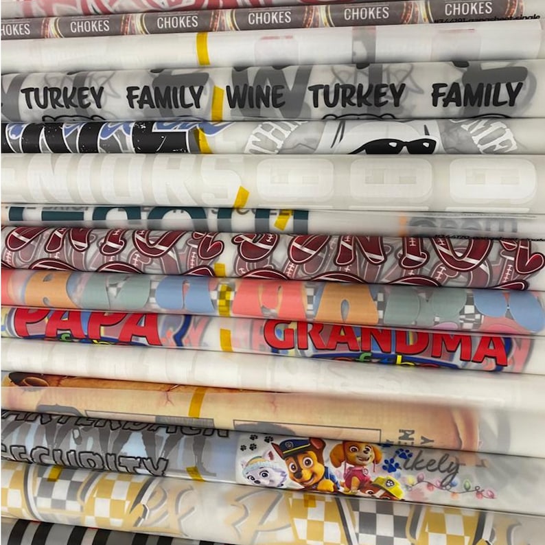 Pu&ograve; includere: Un rotolo di tessuto bianco arrotolato con vari disegni colorati e testo stampato su di essi. Il testo include "TURKEY FAMILY WINE TURKEY FAMILY", "PAPA", "GRANDMA", "SECURITY" e "Likely".