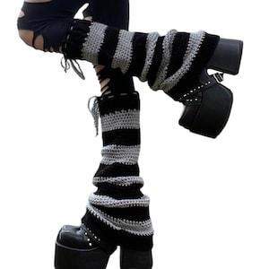 Pu&ograve; includere: Scaldamuscoli a righe nere e grigie. Gli scaldamuscoli sono realizzati in materiale a maglia e sono indossati con stivali con plateau neri. Gli stivali hanno fibbie e borchie. Gli scaldamuscoli sono un accessorio di moda.