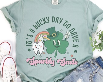 May include: A light blue t-shirt with a green shamrock and a tooth graphic. The text on the shirt reads "It's a lucky day to have a sparkly smile".