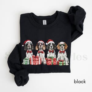 May include: Black Christmas sweatshirt with four dogs wearing Santa hats and sunglasses, each holding a gift box. The dogs are all wearing bow ties.