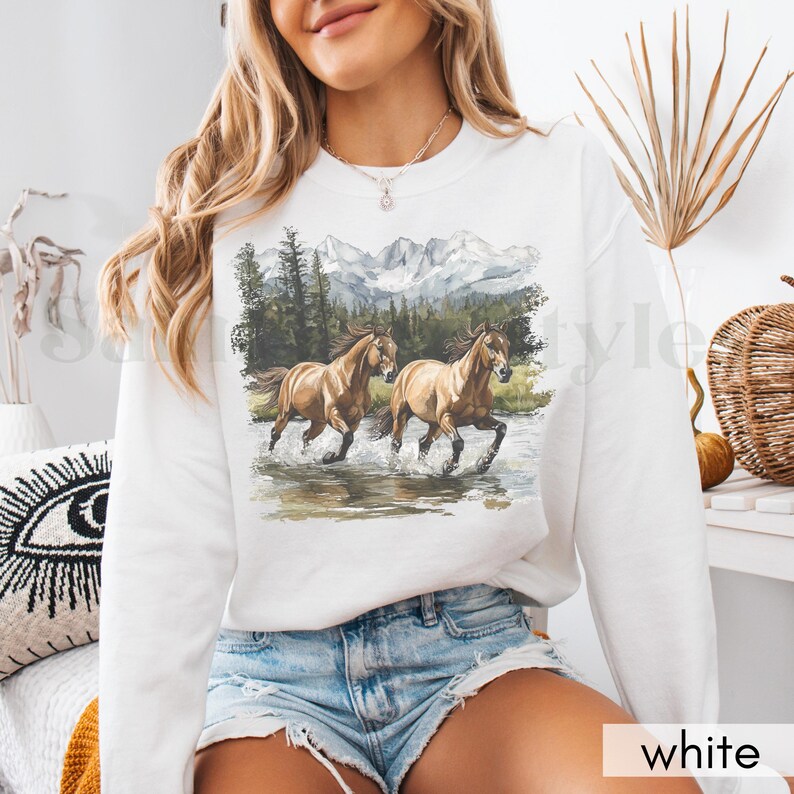 May include: White sweatshirt with a graphic of two brown horses running through a mountain stream. The mountains are snow-capped and the trees are green.