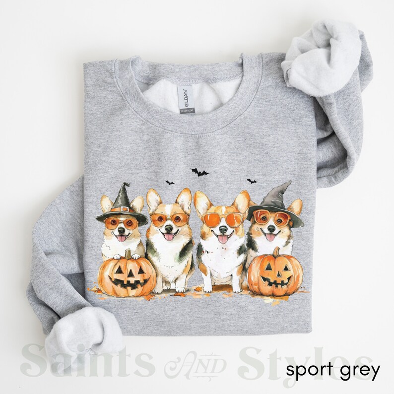 May include: A gray sweatshirt with a graphic of four corgis wearing witch hats and sunglasses, holding jack-o'-lanterns. The corgis are in a row, facing forward. The sweatshirt has a crew neck and long sleeves.