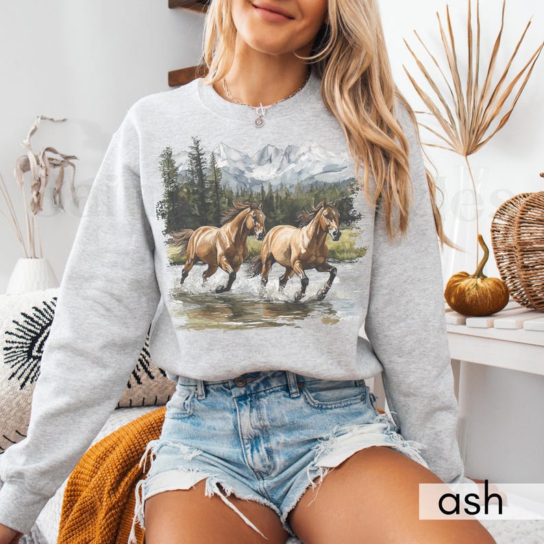 May include: A gray sweatshirt with a graphic print of two brown horses running through a mountain landscape. The sweatshirt has a crew neck and long sleeves.